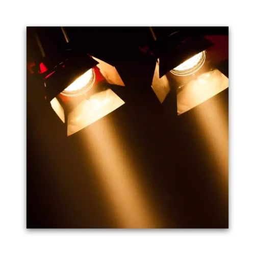 Two stage lighting fixtures emitting warm light beams in a dark setting.