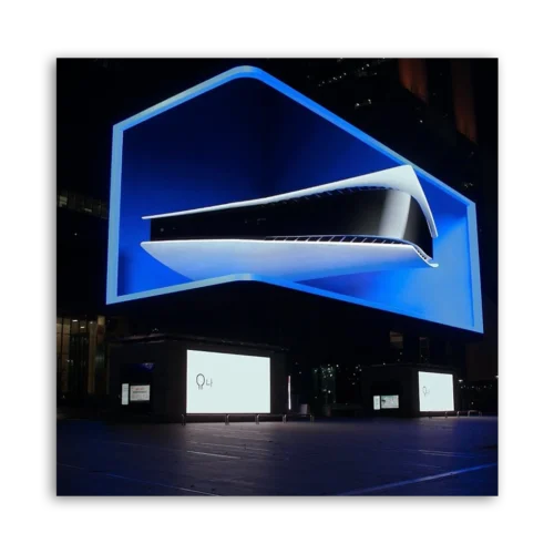 Illuminated display of a PlayStation 5 console on a large screen at night.